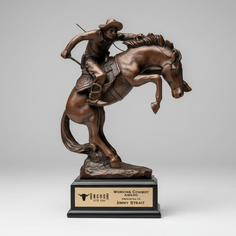 Bronze sculpture of a cowboy on a horse mounted on a wooden post with a rural landscape in the background.