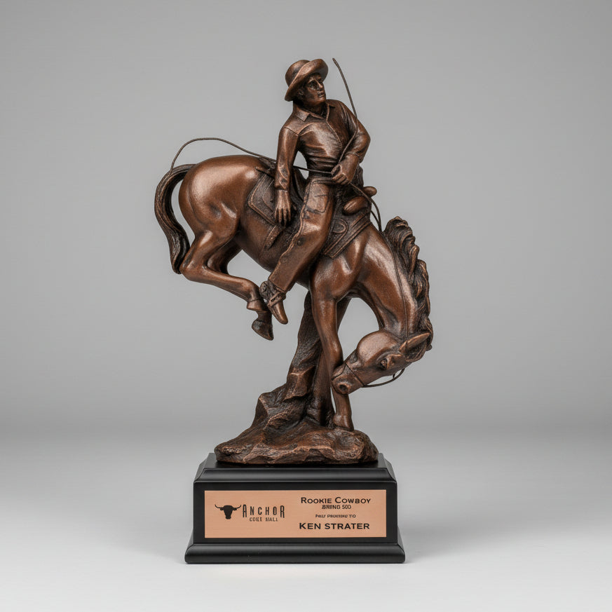 Bronze statue of a cowboy on a horse in a field with a barn and silos in the background.